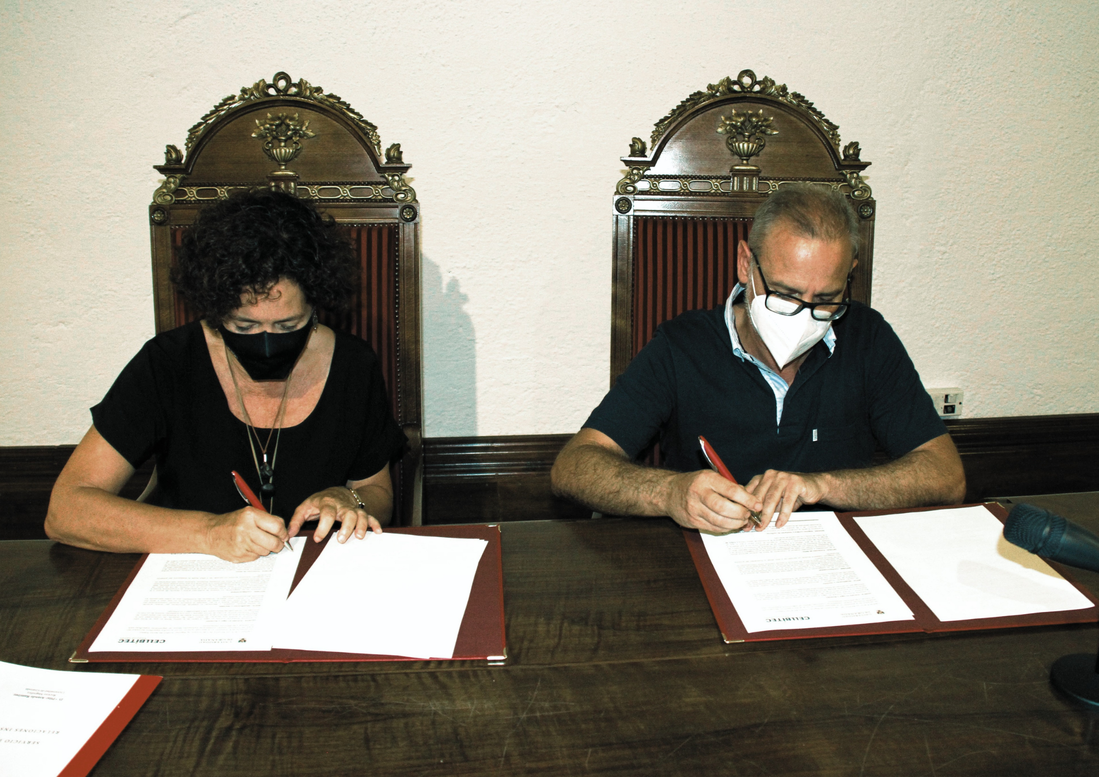 Dos personas sentadas firmando sobre un papel