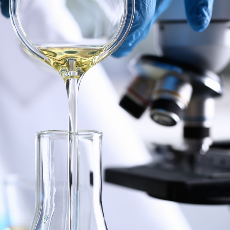 Sesión de presentación Welab Barcelona, innovación en fármacos En un laboratorio se observa un líquido derramándose en un recipiente de ensayo. De fondo un microscopio.